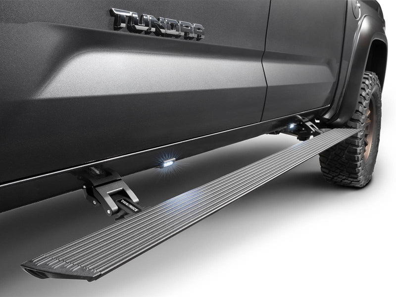 Go Rhino VoltStep: black power running board deployed with lights on under the doors of a gray Toyota Tundra (shown with aftermarket wheels and tires, not included)