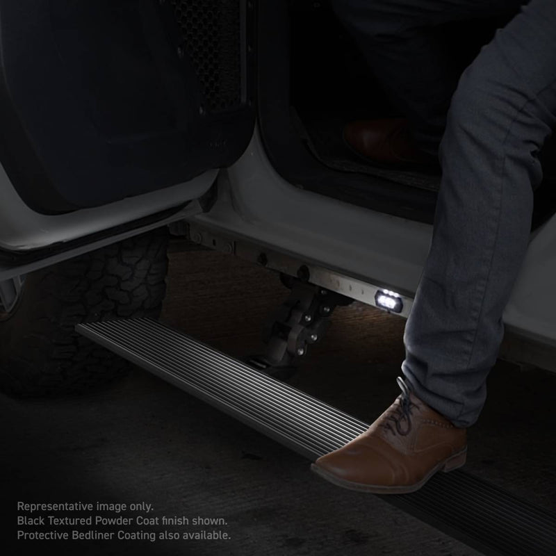 Go Rhino VoltStep: black ribbed power running board deployed under an open door at night, an LED courtesy light lit underneath, a person stepping on it
