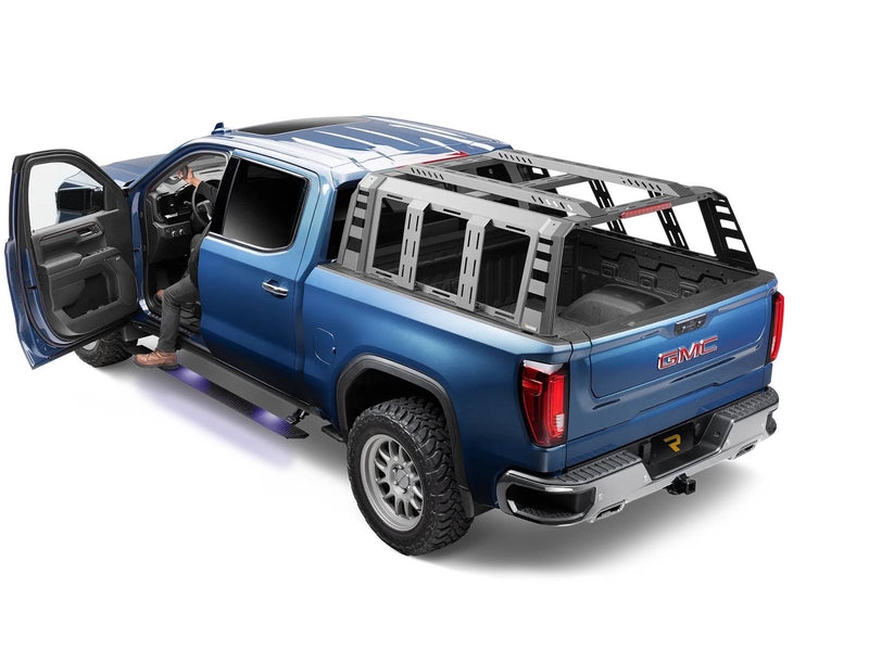 Go Rhino VoltStep: blue GMC Sierra crew cab with front door open and a lit black power running board deployed, a person stepping in (shown with bed rack, aftermarket wheels, not included)