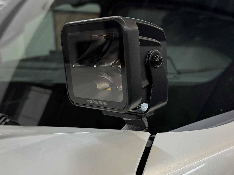 Go Rhino XE: black cube light on a hood bracket at the base of the windshield of a white vehicle (shown with LED cube light, not included)
