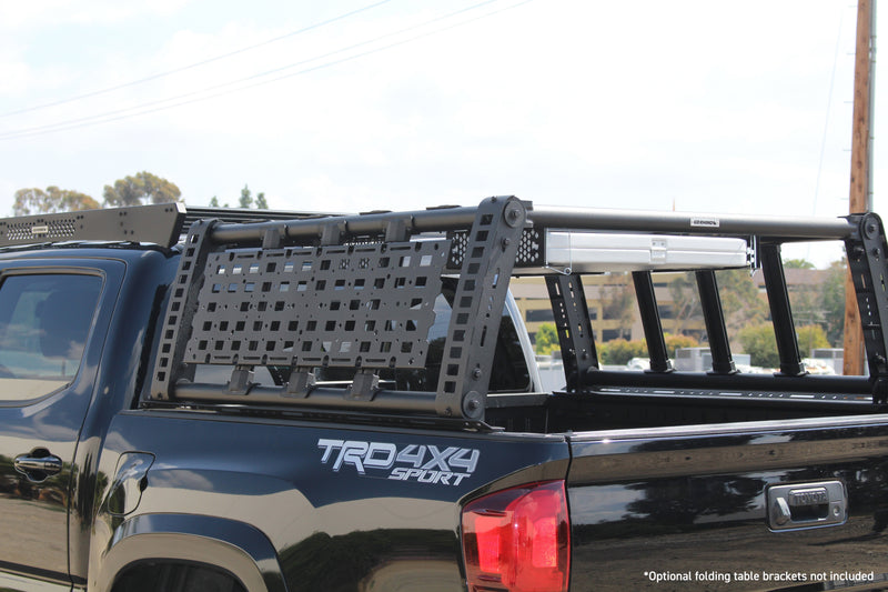 Go Rhino XRS Overland Xtreme: black overland bed rack with a MOLLE panel and roof basket section on a black double cab pickup, a folding table stowed in the rack (shown with folding table and brackets, cab roof basket, not included)