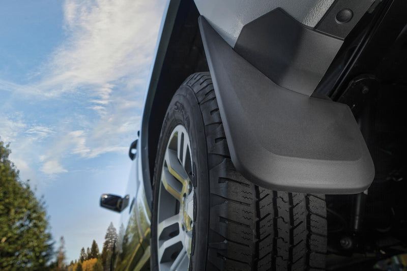 Husky Liners Custom Molded: black molded mud guard mounted behind the rear wheel of a silver pickup, low angle against blue sky