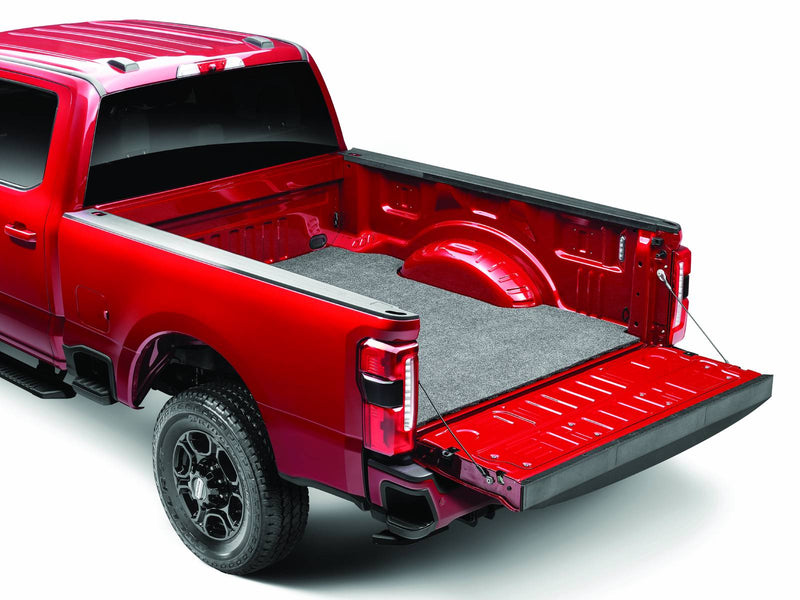 Husky Liners Guardian Comfort: gray carpet bed mat installed on the floor of a red pickup bed with the tailgate down, shown in a Ford F-250/F-350 Super Duty bed (representative image; each mat is cut for its own vehicle)