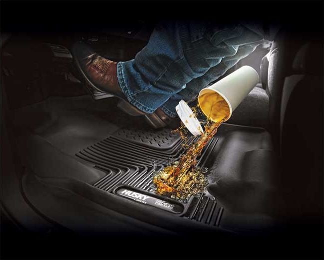 Husky Liners X-act Contour Center Hump Floor Liners: Coffee spilling from a cup onto a black Husky floor liner under a driver's boot
