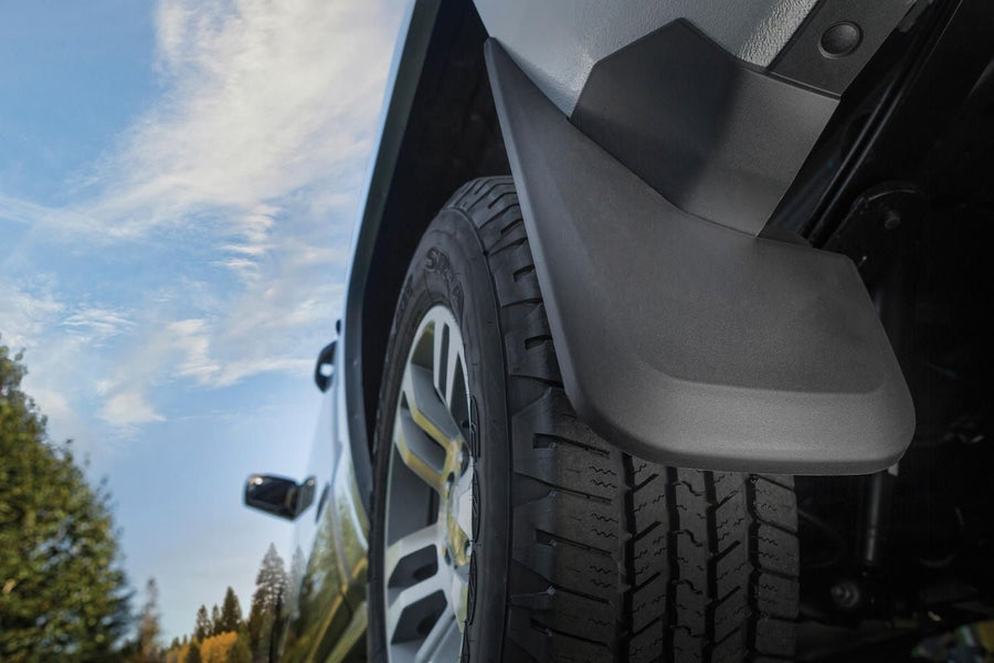 Husky Liners Custom Molded Mud Guards: Black molded mud guard mounted behind the rear wheel of a silver pickup, low angle against blue sky