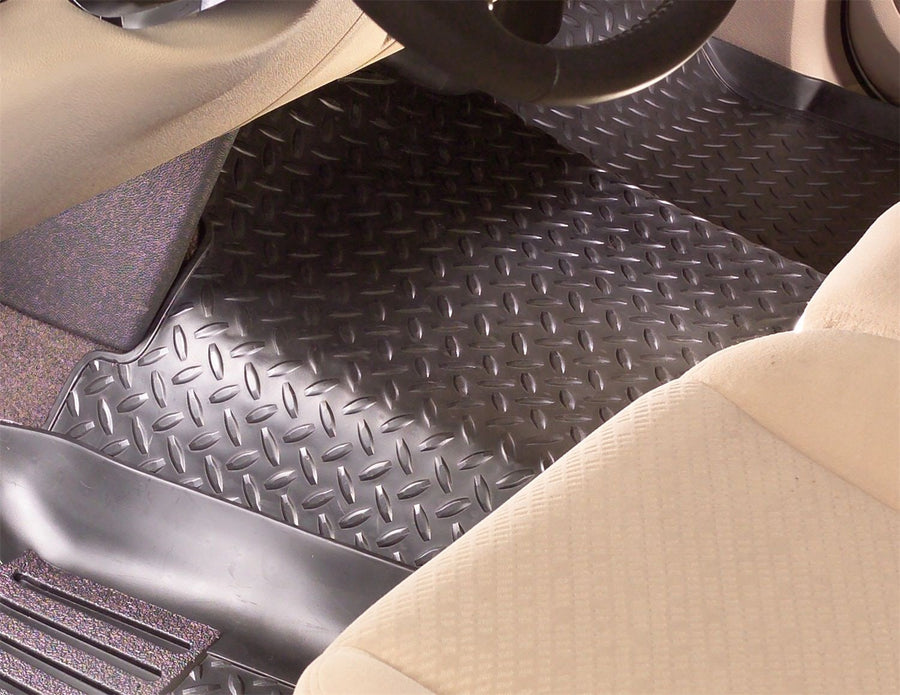 Husky Liners Classic Style Floor Liners: Black diamond-plate floor liner in a driver footwell below the steering wheel, beige seat in foreground