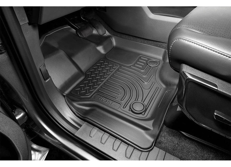 Husky Liners WeatherBeater: black floor liner with curved channels and diamond-plate pad installed on the driver side of a truck below the pedals