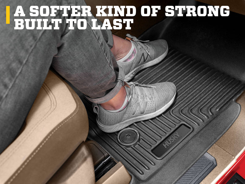 Husky Liners WeatherBeater: feet in gray sneakers resting on a black floor liner beside a tan seat