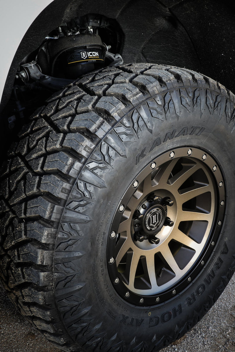 ICON Vehicle Dynamics 2.5 EXP Series Coilover on a Chevrolet Silverado 1500 (listing): front wheel well of a white truck showing a bronze ICON wheel and KANATI all-terrain tire, with the ICON 2.5 EXP coilover top hat visible above