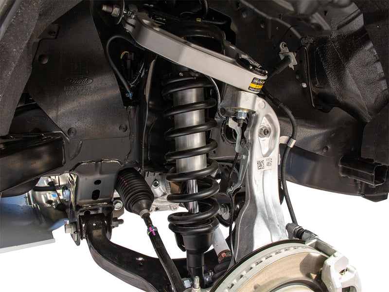 Installed ICON 2.5 coilover with black spring under a silver ICON Delta Joint upper control arm, Ford oval cast into the inner fender.