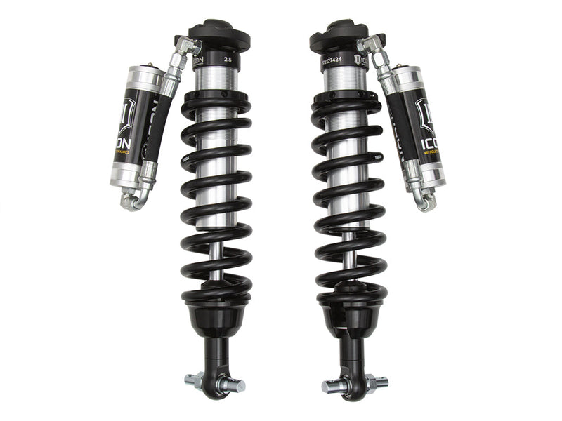 A pair of ICON 2.5 VS remote-reservoir extended-travel coilovers with black springs, silver reservoirs and bar-pin lower mounts, on white.