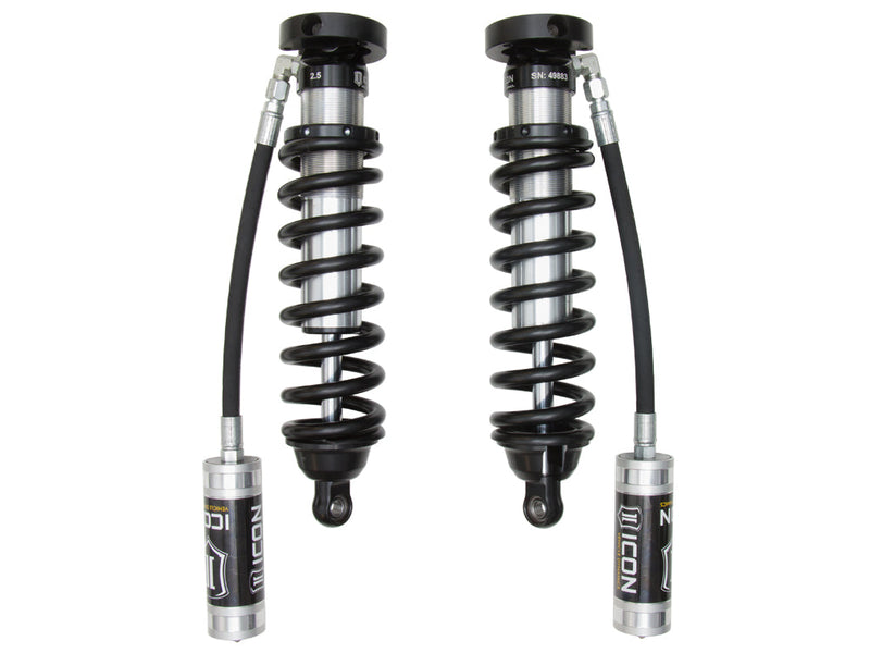 A pair of ICON 2.5 VS remote-reservoir coilovers with black springs and silver ICON reservoirs hanging on long hoses, on white.