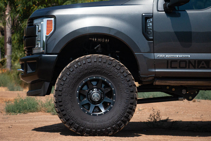 Lifted gray pickup front wheel close-up with a black 8-spoke wheel, off-road tire and suspension link