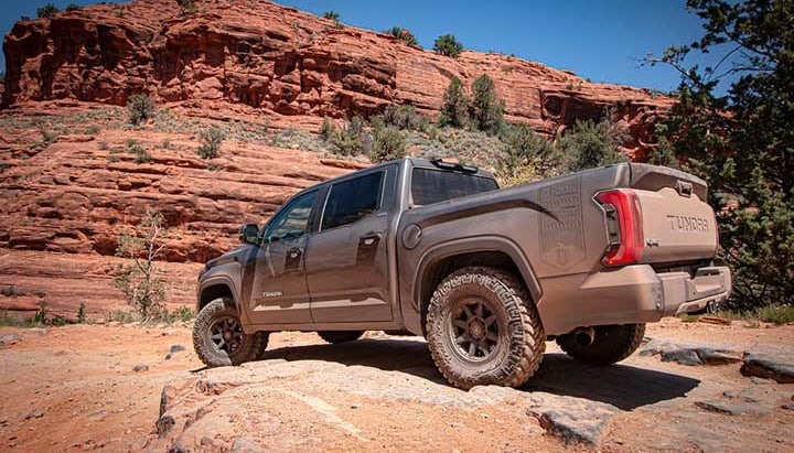A bronze third-generation Toyota Tundra crew cab parked on red sandstone rock, viewed from the rear three-quarter.