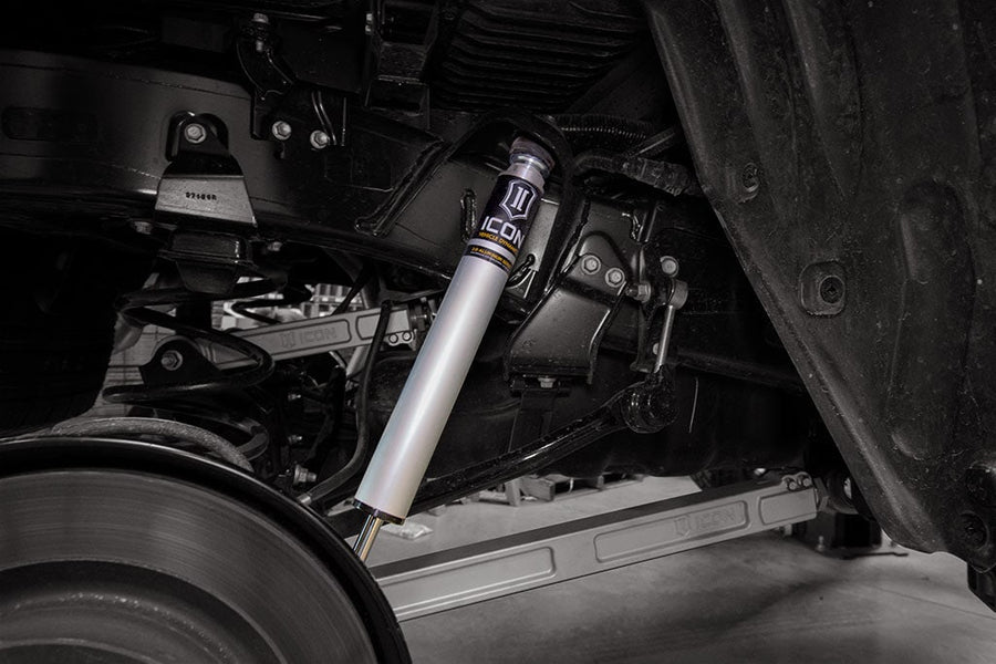 Underbody view of a silver ICON 2.0 aluminum series rear shock installed beside the rear axle, with a coil spring and ICON-marked link bars in view.