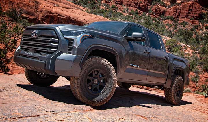 A gray lifted third-generation Toyota Tundra crew cab with black wheels and all-terrain tires on red slickrock.