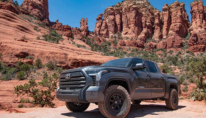 A gray lifted third-generation Toyota Tundra crew cab parked on slickrock beneath red sandstone spires.