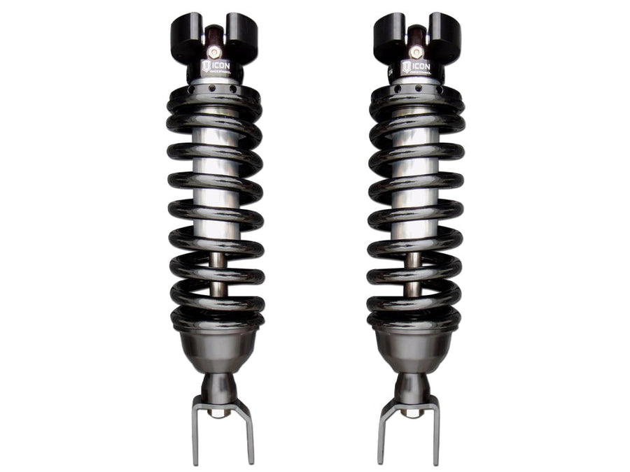 A pair of ICON 2.5 VS coilovers with black springs, top hats and fork lower mounts standing side by side on white.