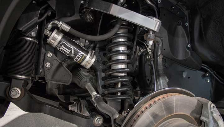 Installed ICON 2.5 remote-reservoir coilover with silver reservoir and black spring under a silver billet upper control arm, brake rotor below.