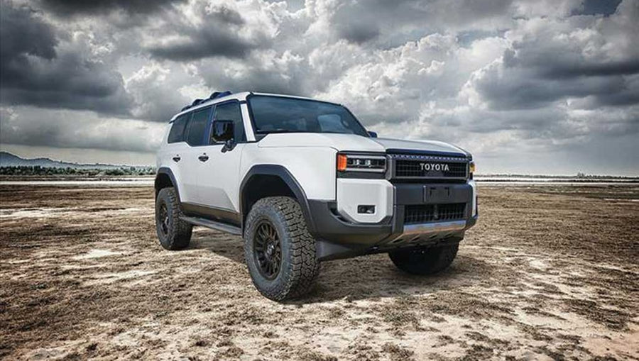 Front three-quarter of a white lifted Toyota Land Cruiser 250 on a cracked mud flat under heavy clouds.