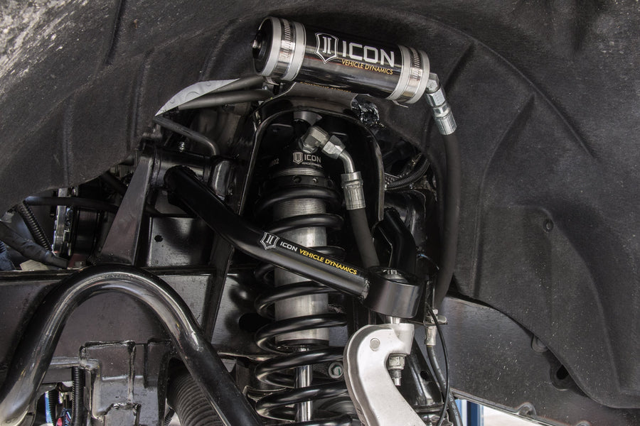 Installed ICON 2.5 remote-reservoir coilover with black spring under a black ICON tubular upper control arm, silver ICON reservoir mounted above.