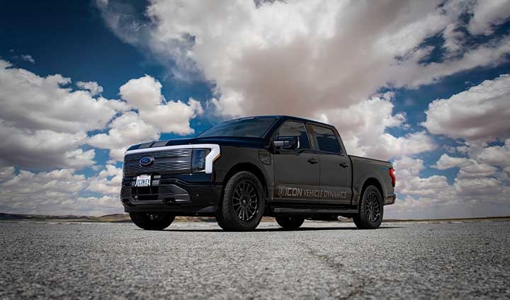 Front three-quarter of a black lowered Ford F-150 Lightning with ICON door lettering on a tarmac lot under clouds.