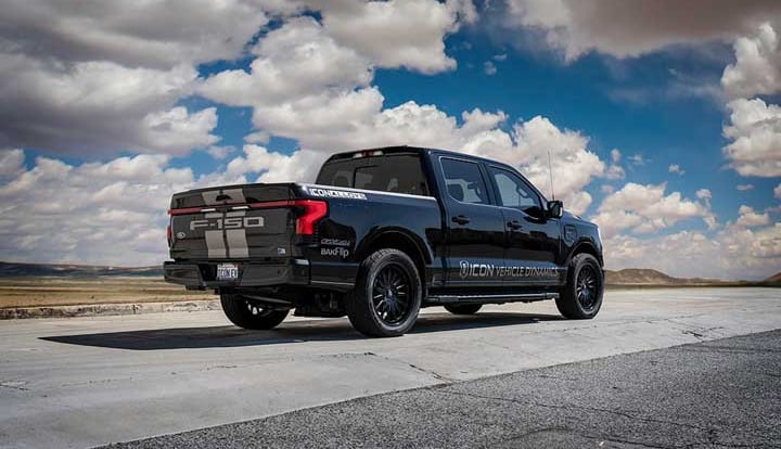 Rear three-quarter of a black lowered Ford F-150 Lightning with F-150 tailgate stripes and ICON side lettering on tarmac.