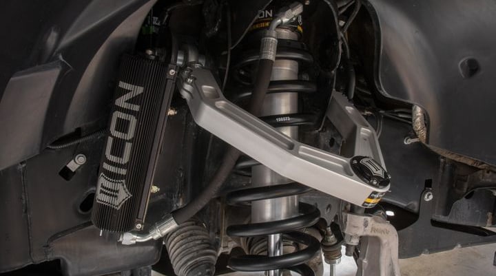 Installed ICON 3.0 remote-reservoir coilover with black spring under a silver billet upper control arm, large finned ICON reservoir mounted in the wheel well.