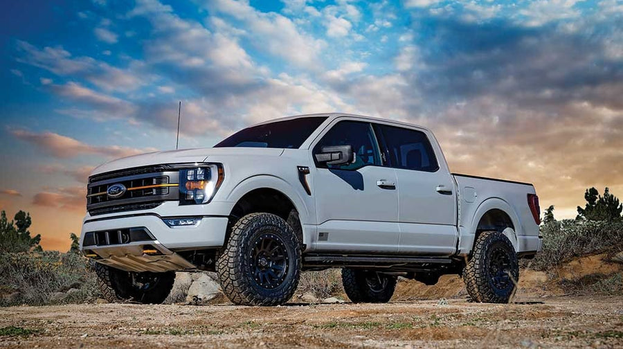 Front three-quarter of a lifted white Ford F-150 crew cab at sunset, Ford grille badge visible.