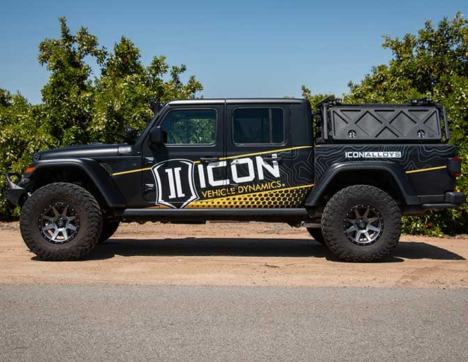 Side profile of a lifted black Jeep Gladiator with ICON livery parked by an orchard.