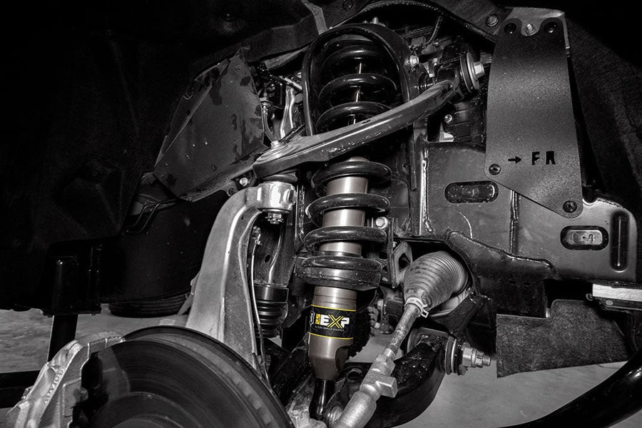 Black-and-white wheel-well view of an installed ICON 2.5 EXP front strut and upper control arm.