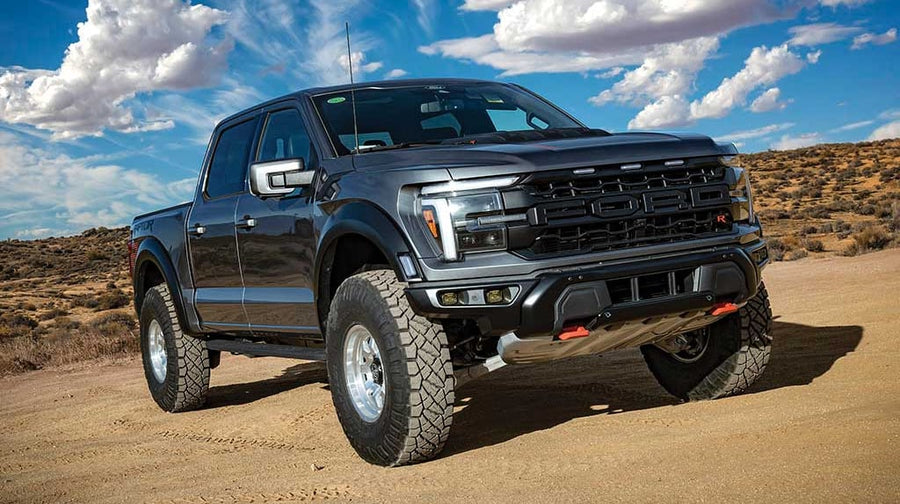 Dark gray third-generation Ford F-150 Raptor, front three-quarter view on desert dirt under a cloudy sky.