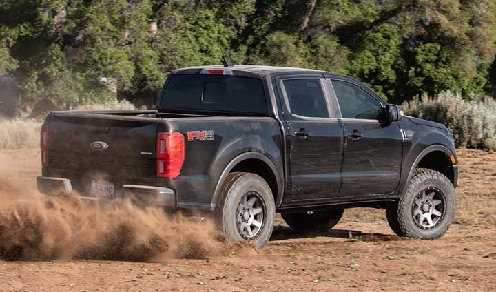 Black lifted Ford Ranger FX4 SuperCrew kicking up dust on a dirt track, rear three-quarter view.