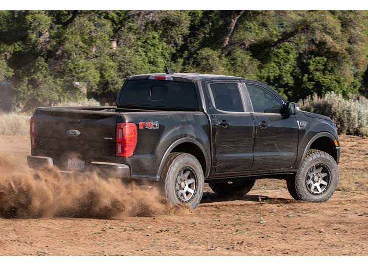 ICON Vehicle Dynamics Stage Suspension System installed on a Ford Ranger, rear three-quarter view: black lifted Ford Ranger FX4 SuperCrew kicking up dust on a dirt track, rear three-quarter view