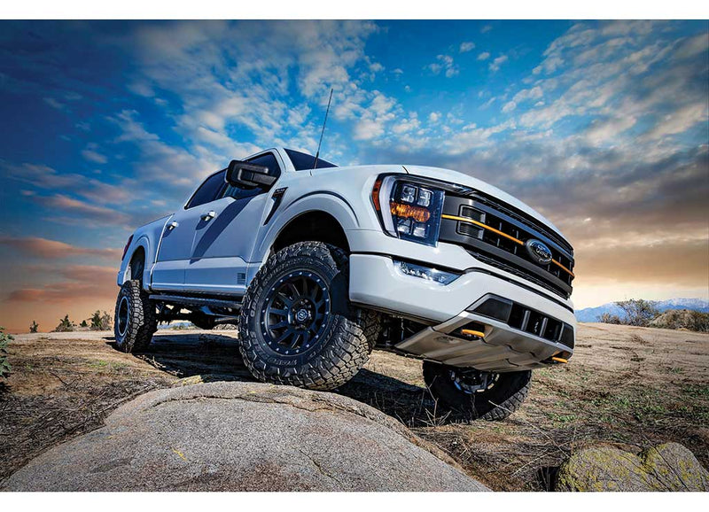 ICON Vehicle Dynamics Stage Suspension System installed on a Ford F-150: low angle of a lifted white Ford F-150 crew cab climbing a rock