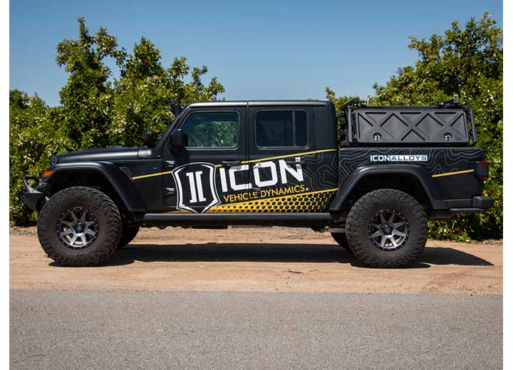 ICON Vehicle Dynamics Stage Suspension System installed on a Jeep Gladiator, side profile view: side profile of a lifted black Jeep Gladiator with ICON livery parked by an orchard