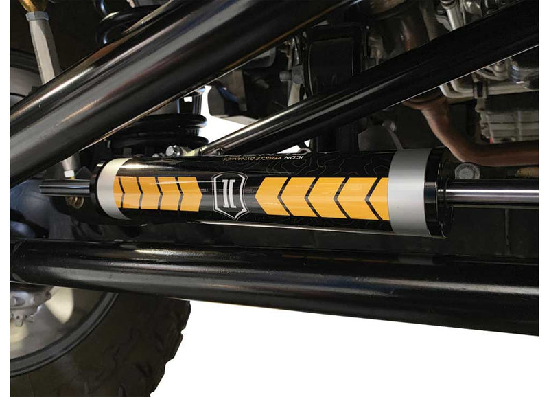 ICON Vehicle Dynamics Ultimate Front End Kit on a vehicle: close-up of an ICON steering stabilizer with orange chevron graphics installed along a tie rod under a vehicle