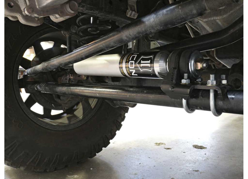 ICON Vehicle Dynamics Ultimate Front End Kit on a vehicle: ICON steering stabilizer installed along the tie rod of a solid front axle, wheel and tire at left