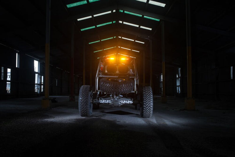 KC HiLiTES 28" Multi-Function Rear-Facing Chase LED Light Bar on a vehicle: rear view of a buggy in a dark warehouse with amber rear lights glowing