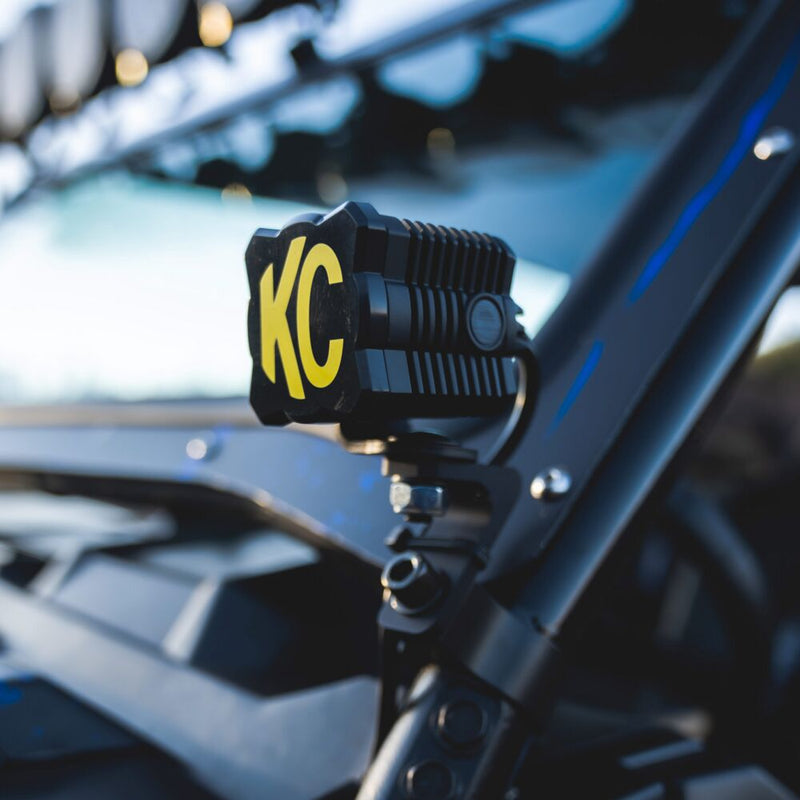 KC HiLiTES FLEX ERA 1 Light Cover & Shield on a vehicle: KC FLEX ERA 1 light with a black and yellow KC cover mounted on a UTV pillar, background blurred