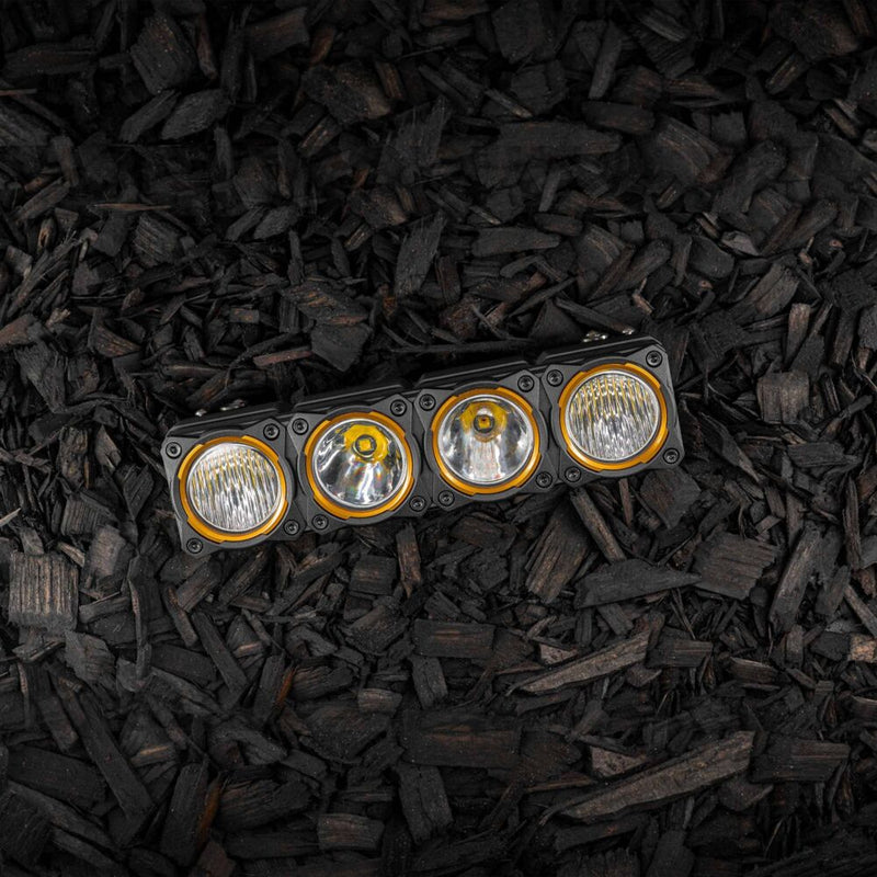 KC HiLiTES FLEX ERA LED Light Bar 10" Segment Bezel Kit on a vehicle: FLEX ERA 10" LED light bar segment fitted with four gold bezel rings, lying on dark wood mulch