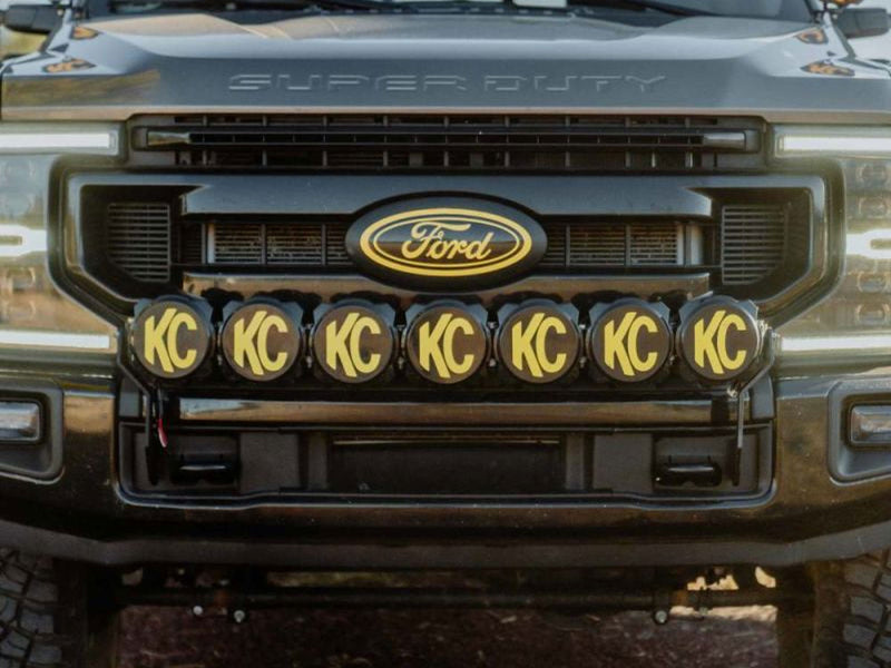 KC HiLiTES Gravity Pro6 45" 7-Light Front Bumper LED Light Bar Kit installed on a Ford Super Duty: front of a dark Ford Super Duty with seven round KC lights wearing black and yellow KC covers mounted in a row below the grille