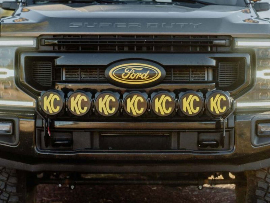 KC HiLiTES Gravity Pro6 45" 7-Light Front Bumper LED Light Bar Kit installed on a Ford Super Duty: front of a dark Ford Super Duty with seven round KC lights wearing black and yellow KC covers mounted in a row below the grille