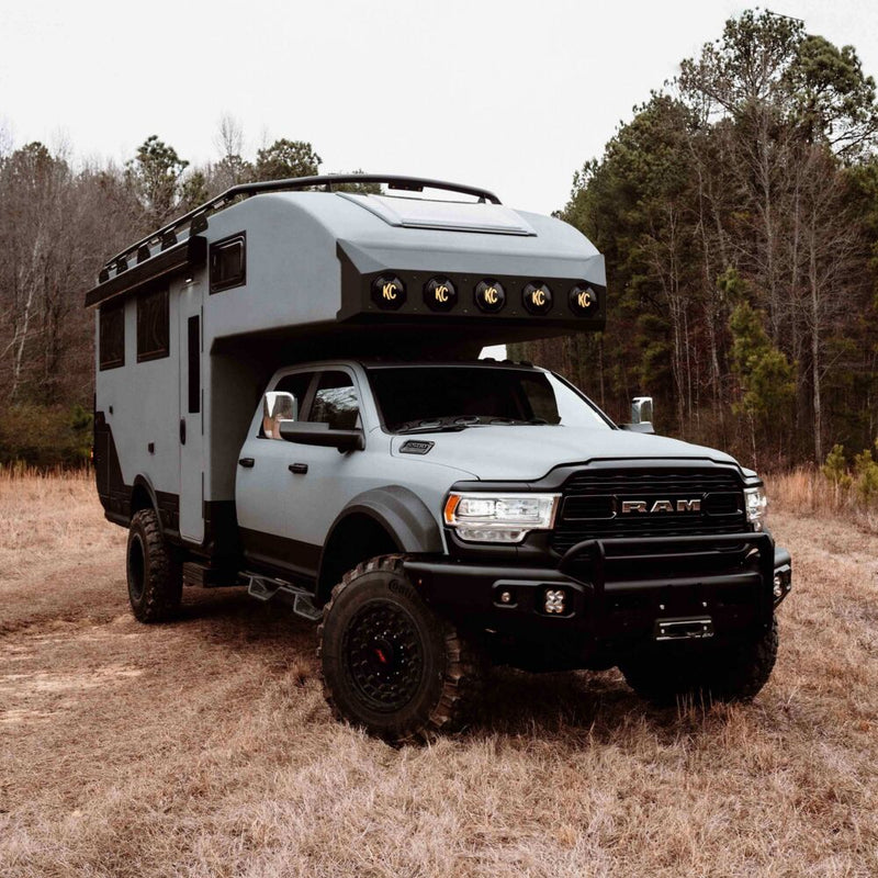 KC HiLiTES SlimLite 8" LED Light Cover & Shield on a Ram 5500: gray Ram 5500 expedition camper in a dry field with five KC covered lights across the cab-over
