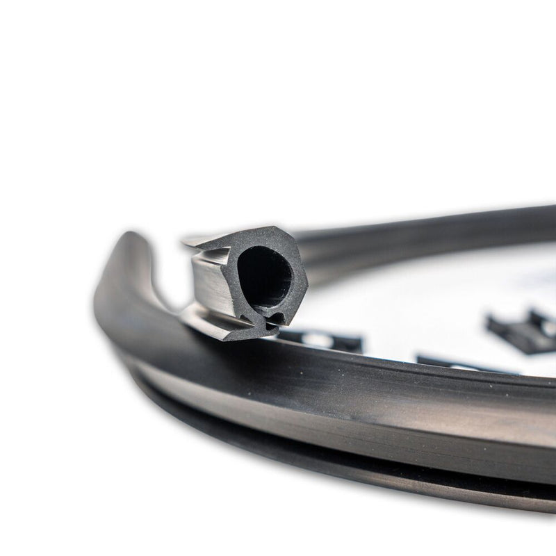 Close-up of the KC HiLiTES Universal Wire Hider with KClips: close-up of the end of a black rubber wire hider strip showing its hollow channel profile, with mounting clips in the background