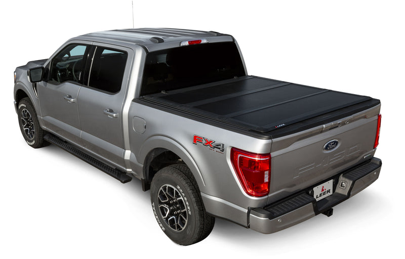 LEER HF350M hard folding tonneau cover on a pickup bed: black hard tri-fold cover closed flat over a silver pickup bed, rear three-quarter view
