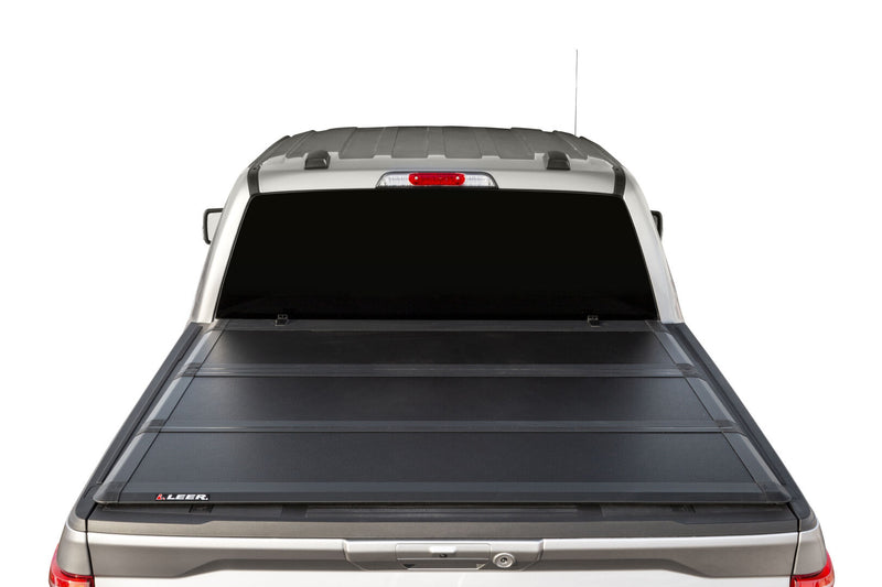 LEER HF350M hard folding tonneau cover on a pickup bed: rear view of a black hard tri-fold cover closed flat over a silver pickup bed; rear window and tailgate top visible