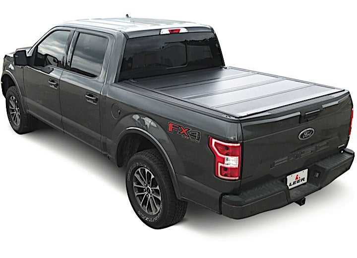 LEER HF650M hard folding tonneau cover on a pickup bed: black hard quad-fold cover closed over a gray pickup bed, rear three-quarter view