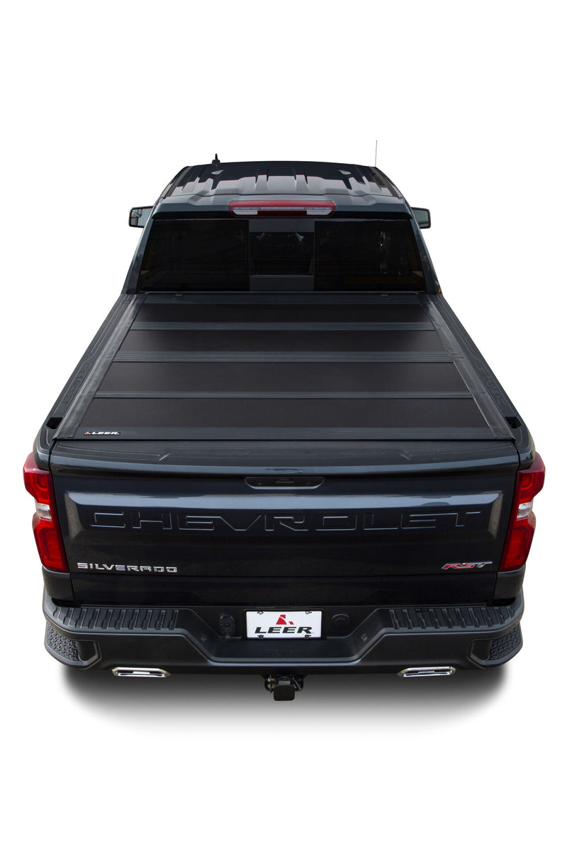 LEER HF650M hard folding tonneau cover on a pickup bed: overhead rear view of a black hard quad-fold cover closed over a dark blue pickup bed