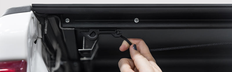 LOMAX Hard Tri-Fold tonneau cover: close-up of a hand pulling the latch release cable under the closed cover of a white truck